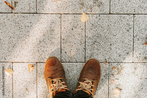 The feet of a man in brown boots on the gray granite sidewalk