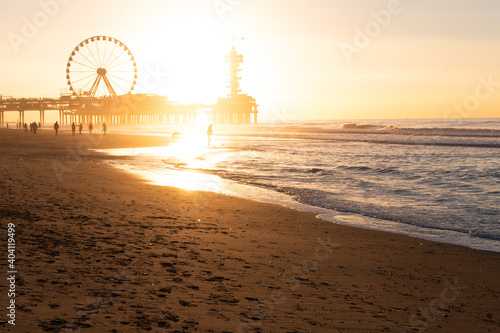 Silhouettes of walking People  at the Beach, with a beautiful Sunset behind a ferris wheel and the pier in scheveningen / netherlands photo