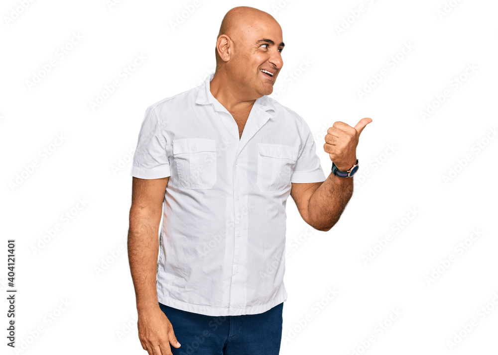Mature middle east man with mustache wearing casual white shirt smiling with happy face looking and pointing to the side with thumb up. Mature middle east man with mustache wearing casual white shirt smiling with happy face looking and pointing to the side with thumb up.