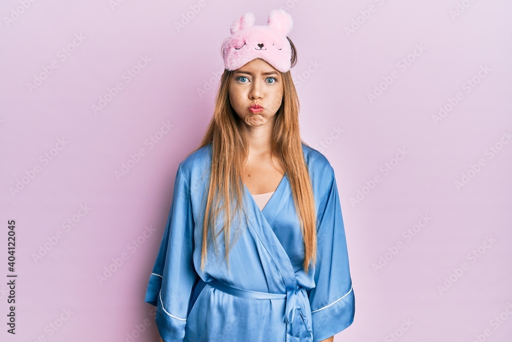 Beautiful young blonde woman wearing sleep mask and pajama puffing cheeks with funny face. mouth inflated with air, crazy expression. Beautiful young blonde woman wearing sleep mask and pajama puffing cheeks with funny face. mouth inflated with air, crazy expression.