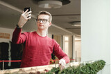 Young man with glasses and with a smartphone in his hands near a glass fence in the mall. Communication concept