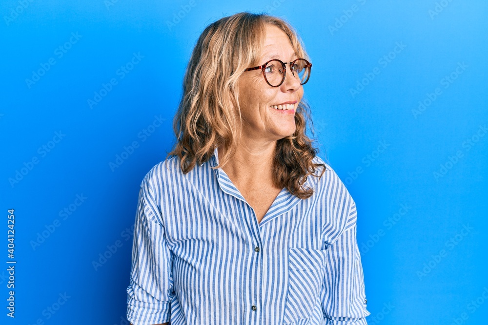 Middle age blonde woman wearing casual clothes and glasses looking away to side with smile on face, natural expression. laughing confident. Middle age blonde woman wearing casual clothes and glasses looking away to side with smile on face, natural expression. laughing confident.