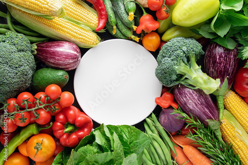 White empty plate on a background of fresh organic vegetables.