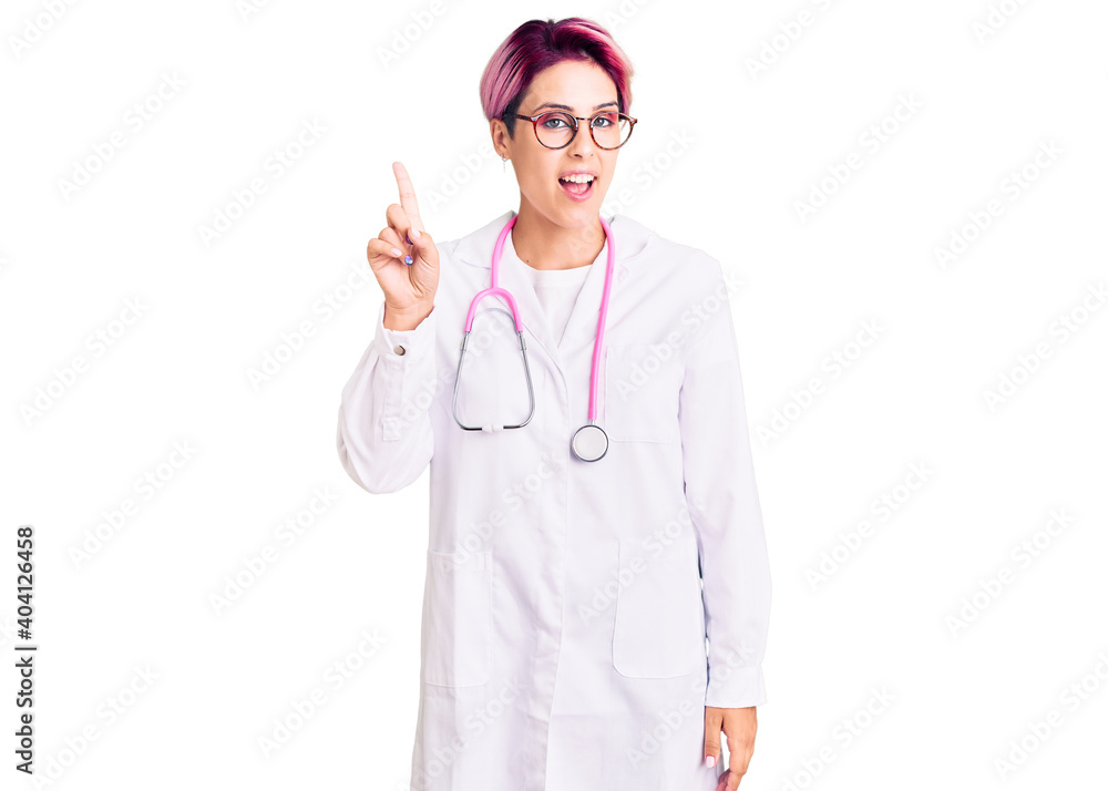 Young beautiful woman with pink hair wearing doctor uniform showing and pointing up with finger number one while smiling confident and happy. Young beautiful woman with pink hair wearing doctor uniform showing and pointing up with finger number one while smiling confident and happy.