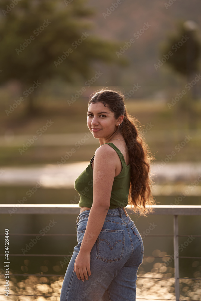 Naklejka premium A beautiful young woman poses for the camera from the back in a mid-length shot in a city center park