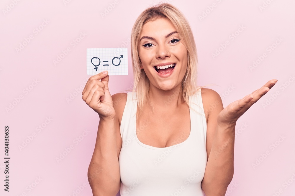 Young blonde woman asking for sex discrimination holding paper with gender equality message celebrating achievement with happy smile and winner expression with raised hand Young blonde woman asking for sex discrimination holding paper with gender equality message celebrating achievement with happy smile and winner expression with raised hand