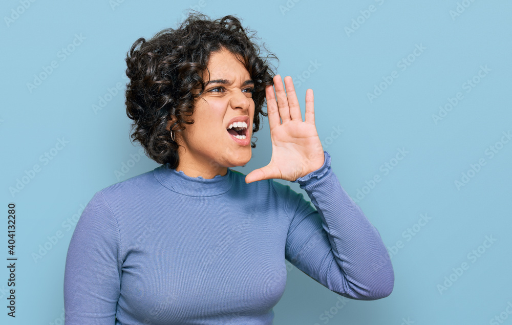 Young hispanic woman with curly hair wearing casual clothes shouting and screaming loud to side with hand on mouth. communication concept. Young hispanic woman with curly hair wearing casual clothes shouting and screaming loud to side with hand on mouth. communication concept.