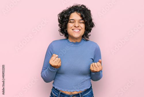 Young hispanic woman with curly hair wearing casual clothes excited for success with arms raised and eyes closed celebrating victory smiling. winner concept.
