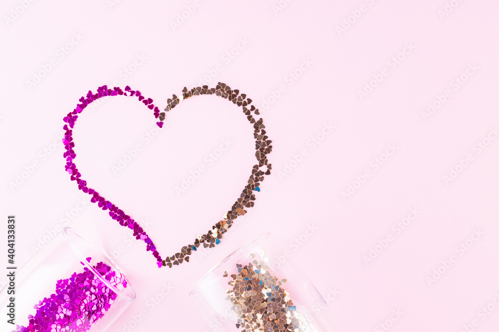 Heart shape made of multicolored glitter. Two champagne glasses with splash of heart shaped confetti over pink background. Valentine's Day concept. Flat lay