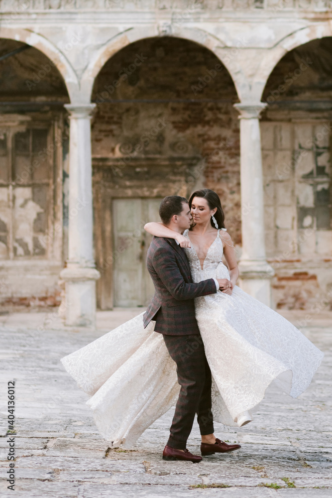 Groom holding bride in his arms on the background of ancient building