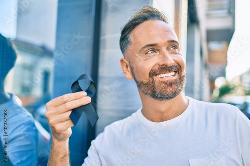Middle age handsome man smiling happy holding black ribbon at the city.