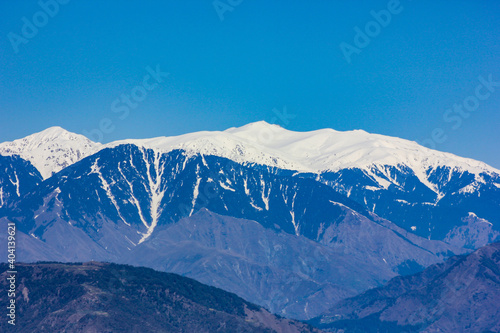 Snow covered peaks of Pir Panjal Mountain Range in Western Himalayas seen from the hill town of Dalhousie in Himachal Pradesh, India, on a bright day with clear blue sky