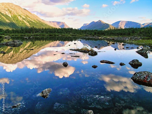 A beautiful mountain valley of glacial origin, lakes with stones and a reflection of the sky, clouds, mountains, a pass, and the northern forest, the Kola Peninsula, Khibiny.