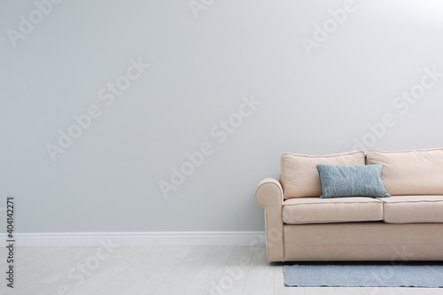 Comfortable beige sofa near light wall indoors  space for text. Simple interior