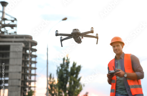 Builder operating drone with remote control at construction site, focus on quadcopter. Aerial survey