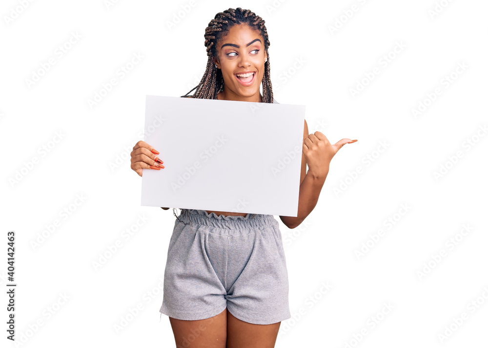 Young african american woman with braids holding blank empty banner pointing thumb up to the side smiling happy with open mouth Young african american woman with braids holding blank empty banner pointing thumb up to the side smiling happy with open mouth