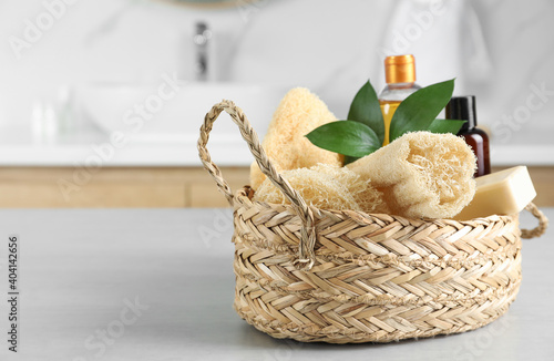 Natural loofah sponges in wicker basket on table indoors. Space for text photo