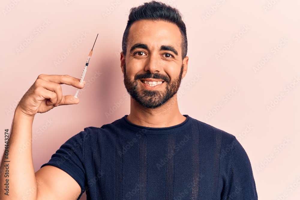 Young hispanic man holding syringe looking positive and happy standing and smiling with a confident smile showing teeth Young hispanic man holding syringe looking positive and happy standing and smiling with a confident smile showing teeth
