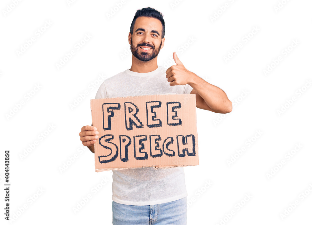 Young hispanic man holding free speech banner smiling happy and positive, thumb up doing excellent and approval sign Young hispanic man holding free speech banner smiling happy and positive, thumb up doing excellent and approval sign