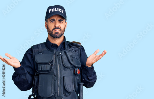 Canvas Print Young hispanic man wearing police uniform clueless and confused with open arms, no idea concept