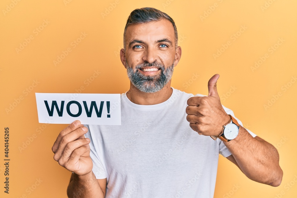 Middle age handsome man holding wow word on paper smiling happy and positive, thumb up doing excellent and approval sign Middle age handsome man holding wow word on paper smiling happy and positive, thumb up doing excellent and approval sign