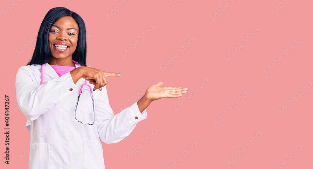 Young african american woman wearing doctor stethoscope amazed and smiling to the camera while presenting with hand and pointing with finger. Young african american woman wearing doctor stethoscope amazed and smiling to the camera while presenting with hand and pointing with finger.