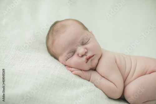 Close up of a sweet newborn infant baby girl laying on a cream-colored neutral blanket with copy space
