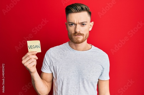 Young redhead man holding sticker with vegan word thinking attitude and sober expression looking self confident © Krakenimages.com