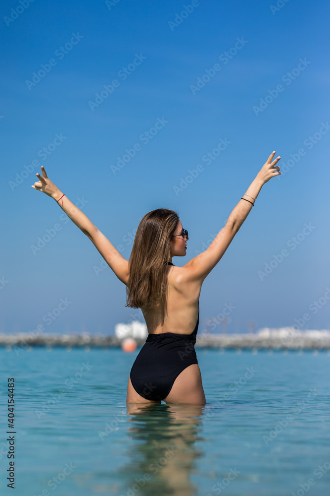 Young beautiful woman inside water on the sunny tropical beach in bikini. Rear view