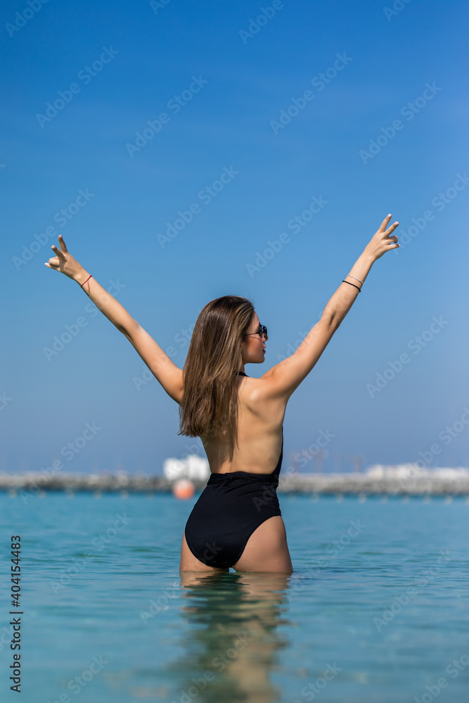 Obraz premium Young beautiful woman inside water on the sunny tropical beach in bikini. Rear view