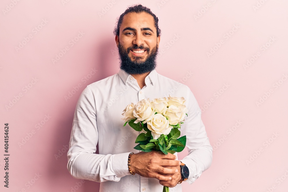 Young arab man holding flowers looking positive and happy standing and smiling with a confident smile showing teeth Young arab man holding flowers looking positive and happy standing and smiling with a confident smile showing teeth