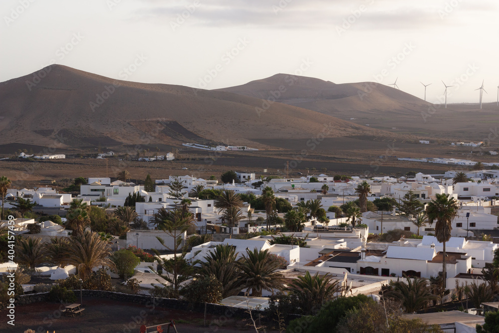 Nazaret town at sunset with volcanic mountains and wind turbines on background. White houses village in Lanzarote island, Spain