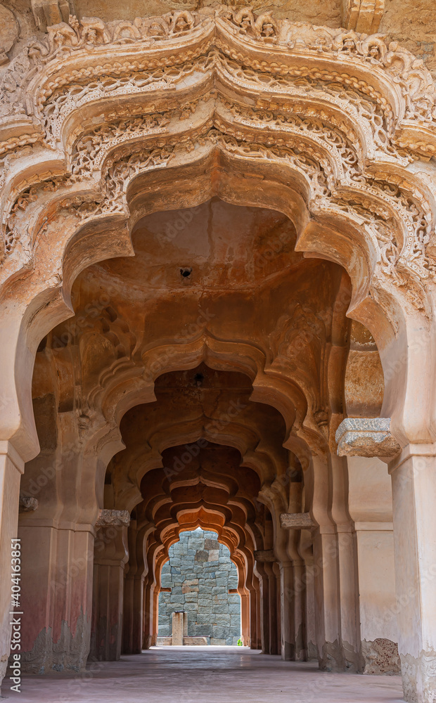 Hampi, Karnataka, India - November 5, 2013: Zanana Enclosure. Looking through a tunnel of arches in Lotus Mahal. Brown stone ending on gray stone wall. Natural light 