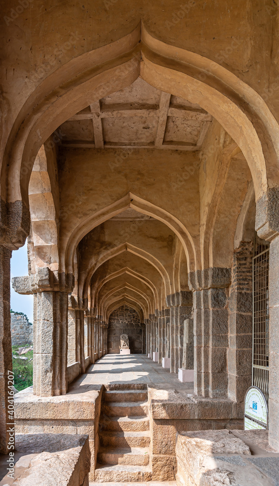 Hampi, Karnataka, India - November 5, 2013: Zanana Enclosure. Long tunnel of arches at archeological items brown-stone exhibition hall, ending on Hanuman statue.