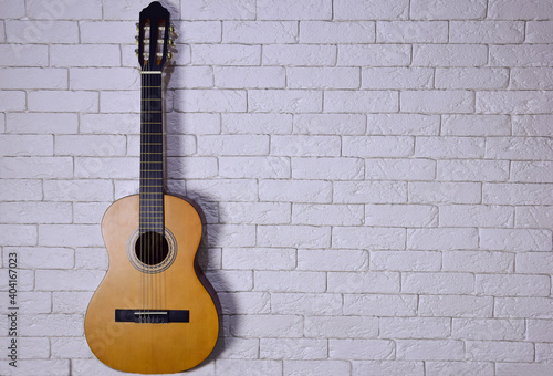 An acoustic guitar stands upright against a light brick wall on the left side. Plenty of space on the right for caption or text © Serhii