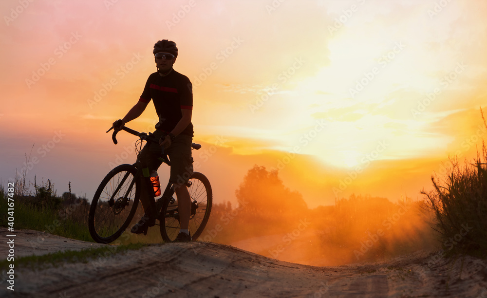 Fototapeta premium Silhouette of cyclist riding on a dust trail at sunset background.