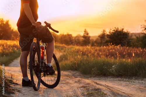 Cyclist standing on dusty trail in the field at sunset.
