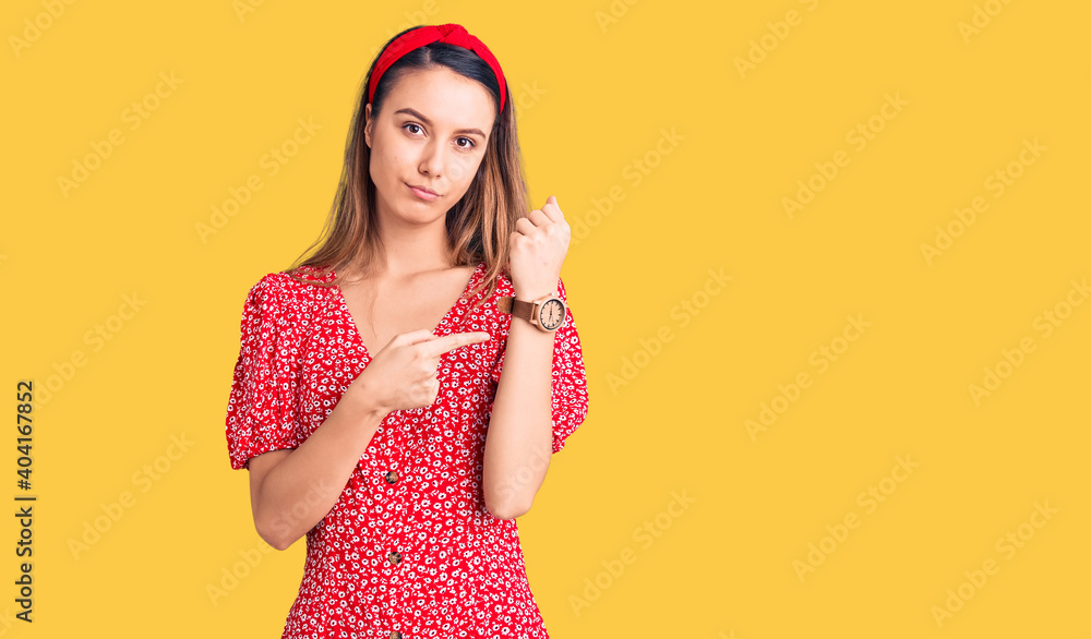 Young beautiful girl wearing dress and diadem in hurry pointing to watch time, impatience, looking at the camera with relaxed expression Young beautiful girl wearing dress and diadem in hurry pointing to watch time, impatience, looking at the camera with relaxed expression
