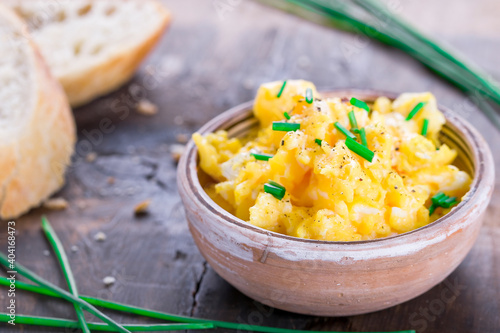  Fresh scrambled eggs with chives in a clay bowl on a wooden table