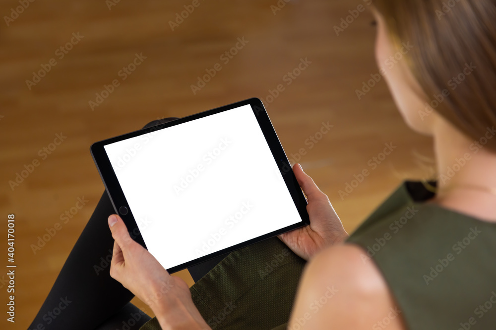 Interested woman sitting and holding tablet with blank white screen in her hands. Back view of a female using large mobile device for reading and analyzing. Interested woman sitting and holding tablet with blank white screen in her hands. Back view of a female using large mobile device for reading and analyzing.