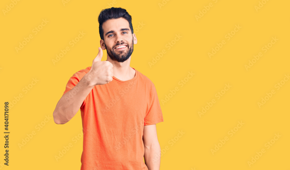 Young handsome man with beard wearing casual t-shirt doing happy thumbs up gesture with hand. approving expression looking at the camera showing success. Young handsome man with beard wearing casual t-shirt doing happy thumbs up gesture with hand. approving expression looking at the camera showing success.