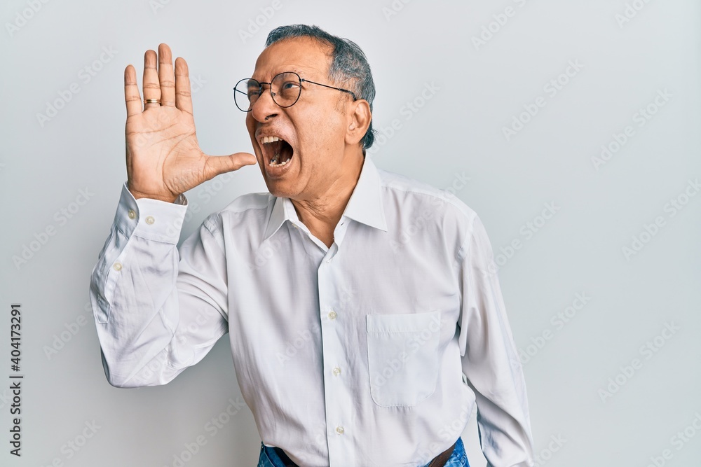 Middle age indian man wearing casual clothes and glasses shouting and screaming loud to side with hand on mouth. communication concept. Middle age indian man wearing casual clothes and glasses shouting and screaming loud to side with hand on mouth. communication concept.