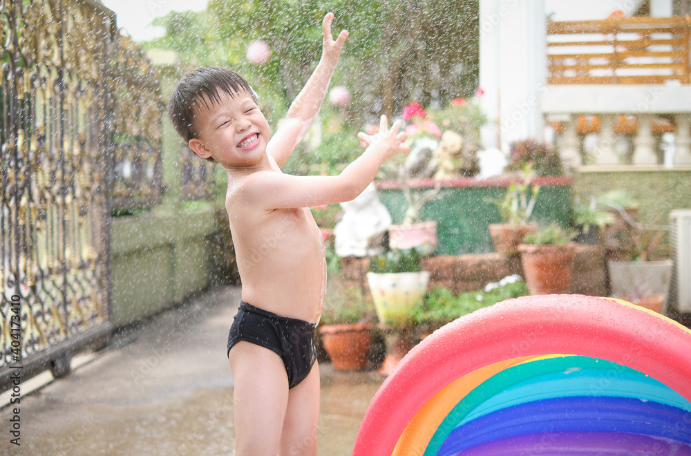 Obraz premium Cute little smiling Asian 4 - 5 years old toddler boy child having fun playing with splash water in the garden at home in the sunny morning, Hot summer day concept