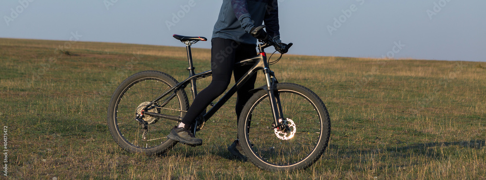 Fototapeta premium Cyclist in shorts and jersey on a modern carbon hardtail bike with an air suspension fork standing on a cliff against the background of fresh green spring forest