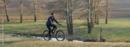 Cyclist in shorts and jersey on a modern carbon hardtail bike with an air suspension fork standing on a cliff against the background of fresh green spring forest