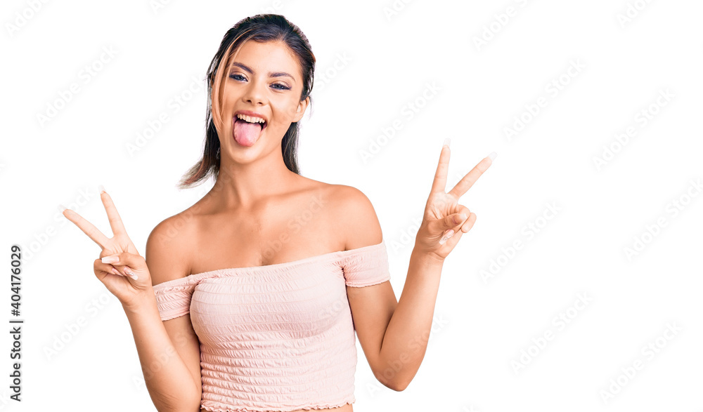 Young beautiful woman wearing casual clothes smiling with tongue out showing fingers of both hands doing victory sign. number two. Young beautiful woman wearing casual clothes smiling with tongue out showing fingers of both hands doing victory sign. number two.