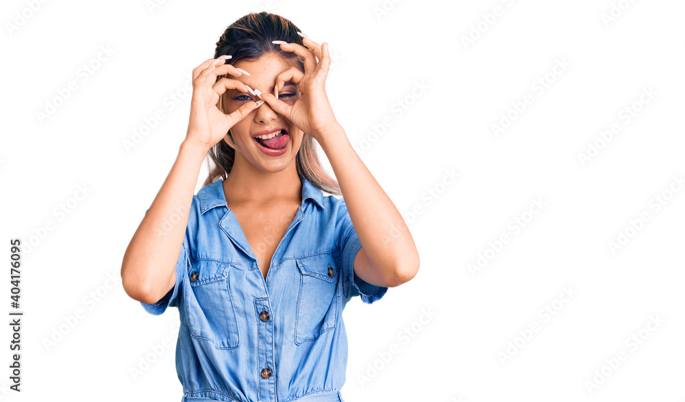Young beautiful woman wearing casual clothes doing ok gesture like binoculars sticking tongue out, eyes looking through fingers. crazy expression. Young beautiful woman wearing casual clothes doing ok gesture like binoculars sticking tongue out, eyes looking through fingers. crazy expression.