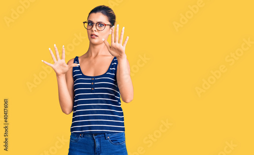 Young beautiful woman wearing casual clothes and glasses afraid and terrified with fear expression stop gesture with hands, shouting in shock. panic concept.