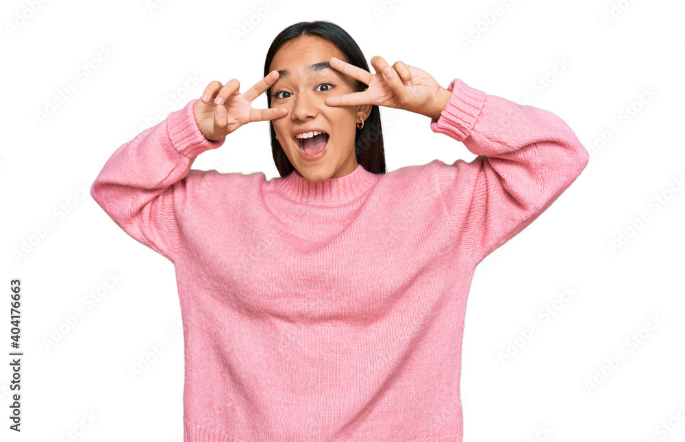 Young asian woman wearing casual winter sweater doing peace symbol with fingers over face, smiling cheerful showing victory Young asian woman wearing casual winter sweater doing peace symbol with fingers over face, smiling cheerful showing victory
