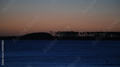 View of Gorriti Island at dusk, seen from Mansa Beach during a warm sunset. The shape of the trees can be seen in the horizon. photo